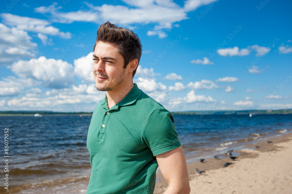 Young man wearing polo looking away at the beach under scenic cloudy sky on sunny day Young man wearing polo looking away at the beach under scenic cloudy sky on sunny day