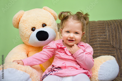 Little girl with big teddy bear sitting on sofa in the living room.