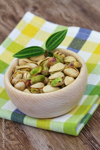 Pistachio nuts in wooden bowl on checkered cloth 