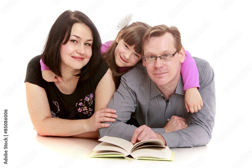 Happy family mom dad and daughter reading a book lying on the fl