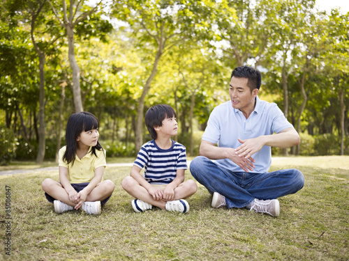 asian father and children talking in park