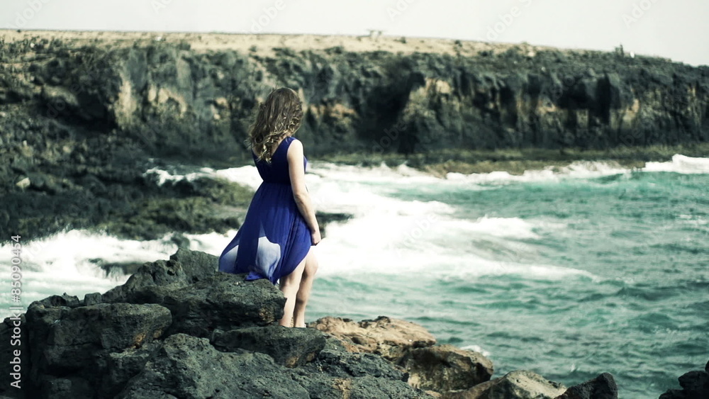 Lonely woman standing on rocks near sea, slow motion shot at 240fps 

