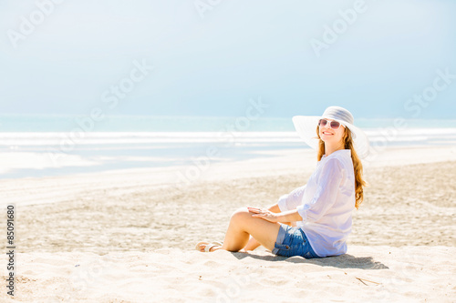 Beautifil young woman sitting on the beach at sunny day enjoing