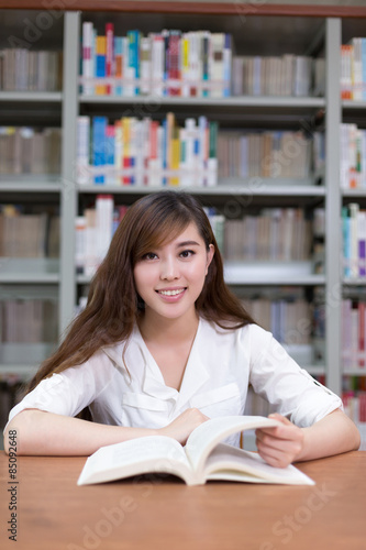 Beautiful asian female student read book in library with bookshe