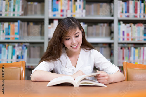 Beautiful asian female student read book in library with bookshe