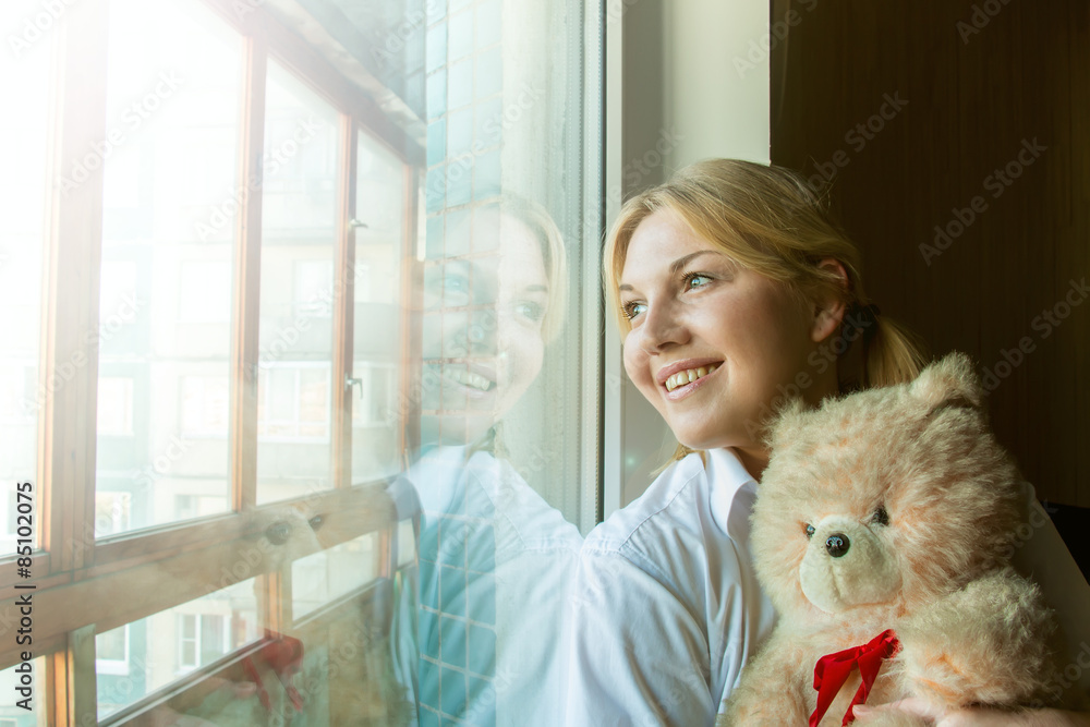 A woman by the window with a teddy bear. A woman by the window with a teddy bear.