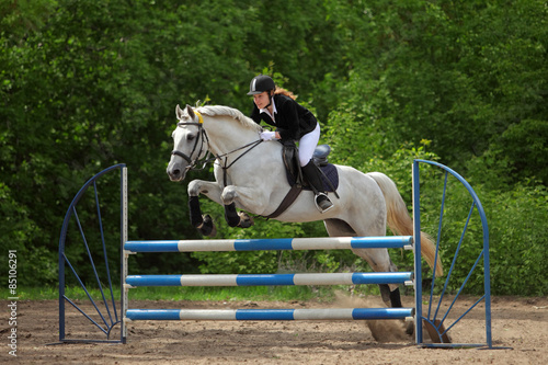 Young equestrian rider jumping over obstacle