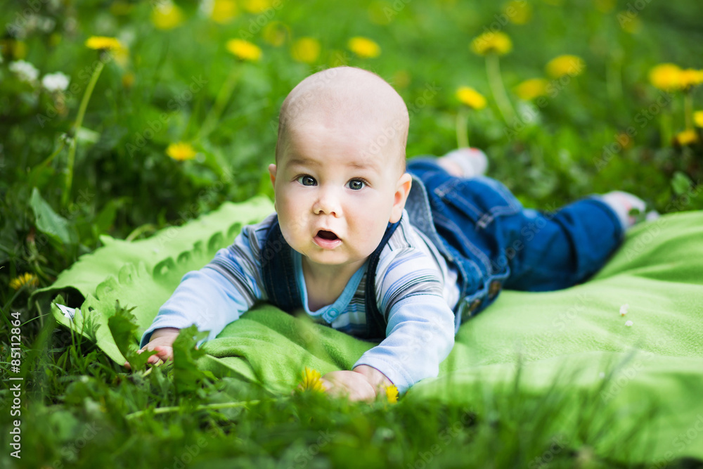 Charming infant in jeans coveralls lying on the lawn in the summer park Charming infant in jeans coveralls lying on the lawn in the summer park