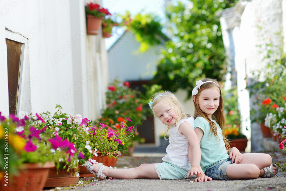Two adorable little sisters sitting among flowers Two adorable little sisters sitting among flowers