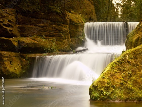 Stony weir on small mountain river. Stream is flowing over blocks and makes milky water.