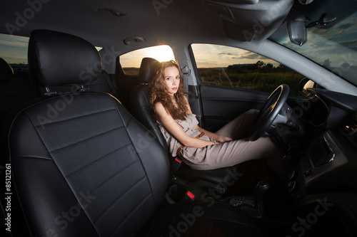Beautiful young girl sitting in a car and looking at the camera outdoors