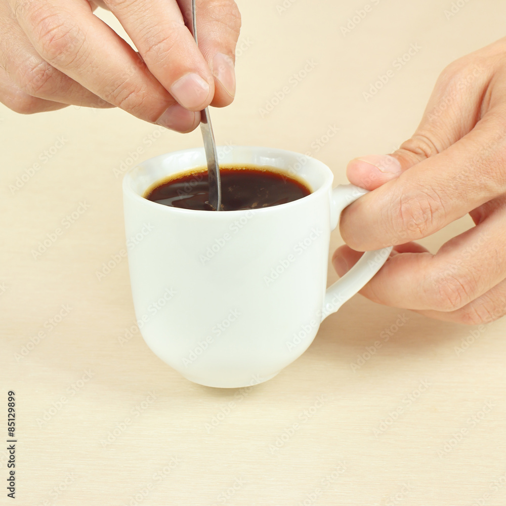 Hands mixing with a spoon of black coffee in the cup Hands mixing with a spoon of black coffee in the cup