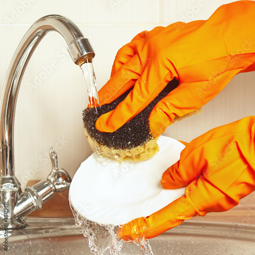 Hands in rubber gloves with sponge wash the dishes under running water photo