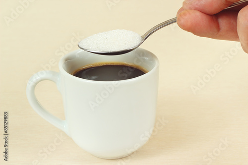 Hand pours sugar from a spoon in a coffee cup