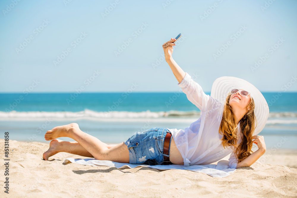 Beautifil young woman lying on the beach at sunny day and taking