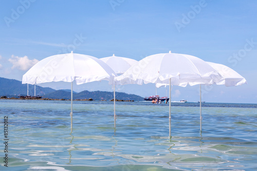 White umbrella on summer tropical beach with sailing boat.
