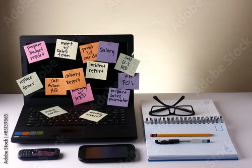 Laptop computer with messages on colorful papers, cellphone, smartphone, notebook, pen, pencil and eyeglasses