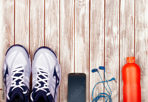 Sport equipment. Sneakers, water, earphones and phone on wooden