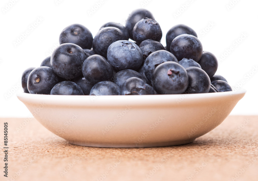 Blueberry in a white bowl on cork board background Blueberry in a white bowl on cork board background