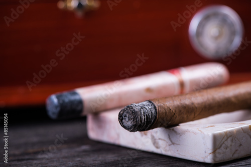Cuban cigar in marble ashtray and wooden humidor