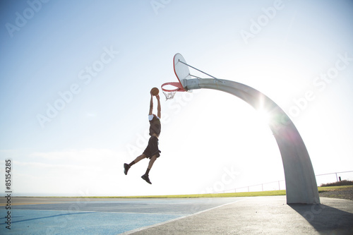 Man dunking basketball into hoop against clear sky†