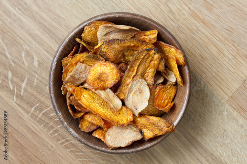 Fried carrot and parsnip chips in rustic wood bowl. From above.