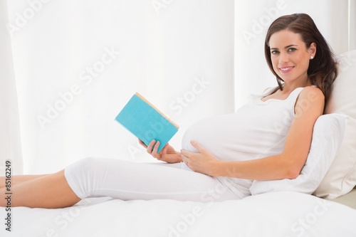 Smiling pregnancy reading in his bed