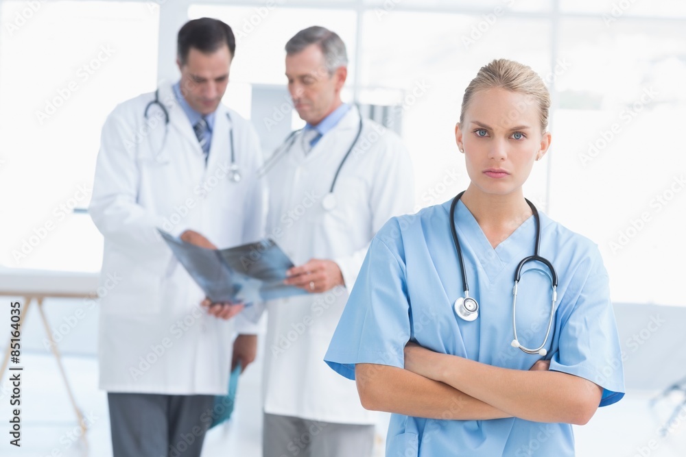 Irritated doctor looking at camera while her colleagues works Irritated doctor looking at camera while her colleagues works
