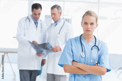 Irritated doctor looking at camera while her colleagues works 