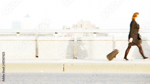 Bleached video footage of London commuters during early morning rush hour on London Bridge with traffic streaming by the foreground.