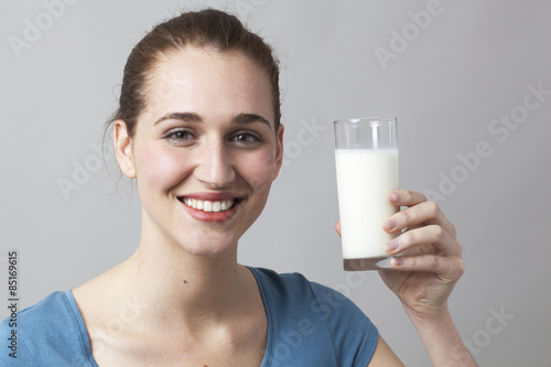 smiling young woman enjoying holding a glass of milk or any white beverage for freshness