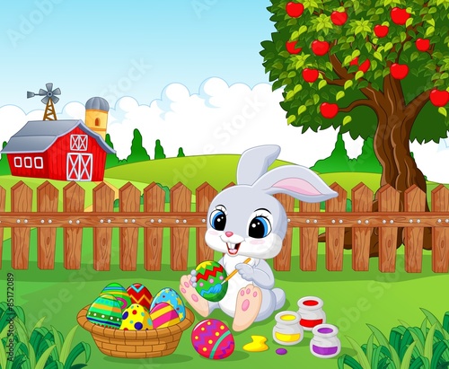 Cute Easter Bunny painting an egg in the garden