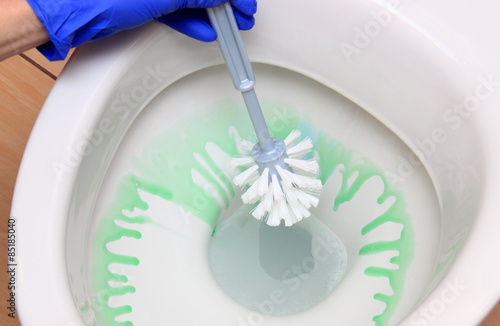 Hand of woman in blue glove cleaning toilet bowl