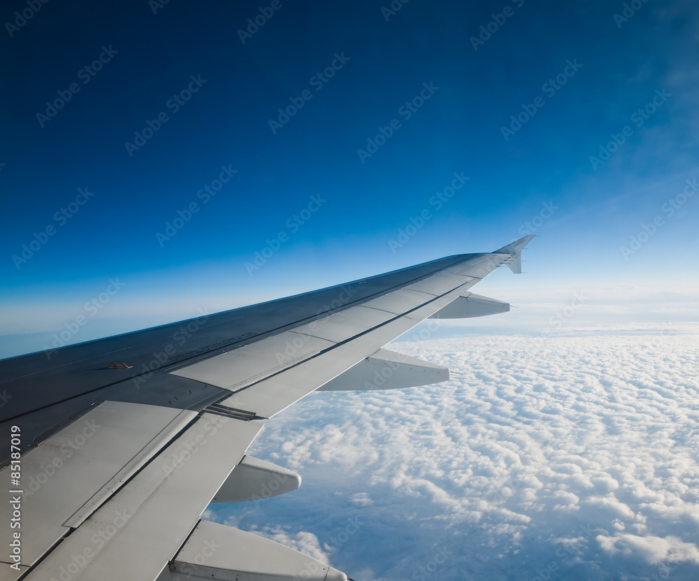 Wing of airplane flying above the clouds in the sky Wing of airplane flying above the clouds in the sky