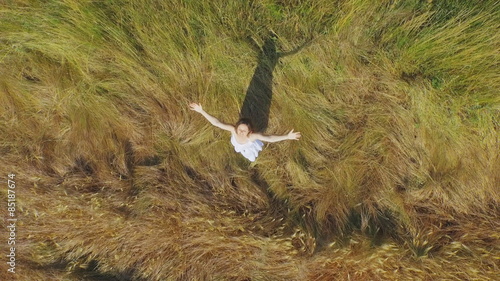 Beautiful young woman with a long white dress standing in a field of long grass lifting her arms up with joy of being surrounded  by natural beauty.