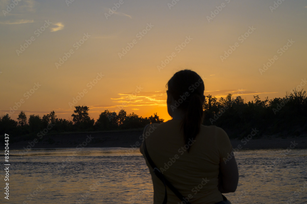 Fototapeta premium Silhouette of a woman while observe sunset by the river