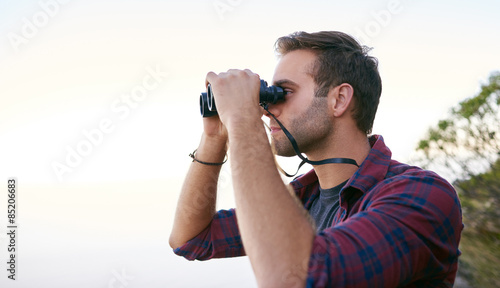 Young man looking into the distance with binoculars