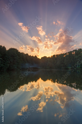 Beautiful summer sunset with rays on a pond in the forest park