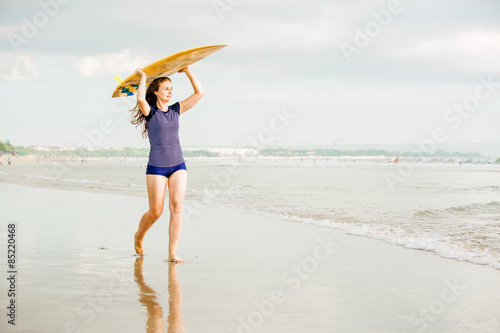 Beautiful sexy surfer girl on the beach at sunset walks along