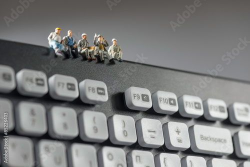 Miniature workers sitting on top of keyboard. Technology concept photo