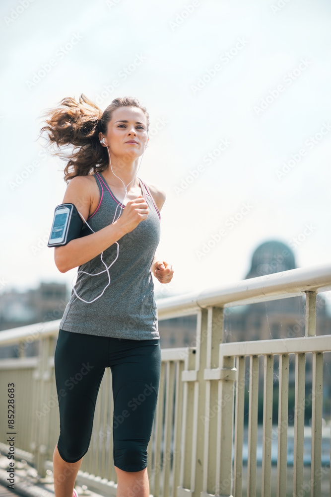 Long-haired woman jogging on bridge listening to music in summer
