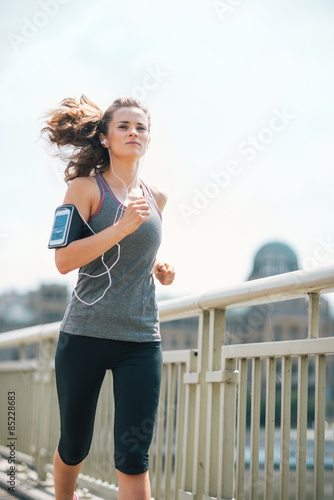 Fototapeta Naklejka Na Ścianę i Meble -  Long-haired woman jogging on bridge listening to music in summer