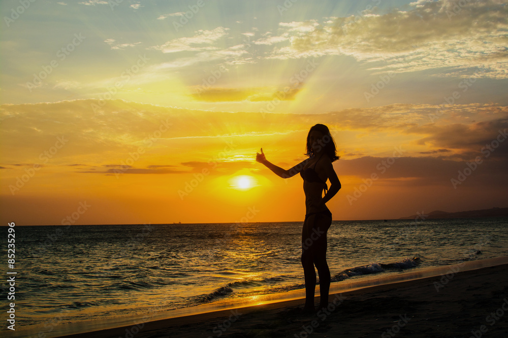 Silhouette of young woman on the beach at sunset sky