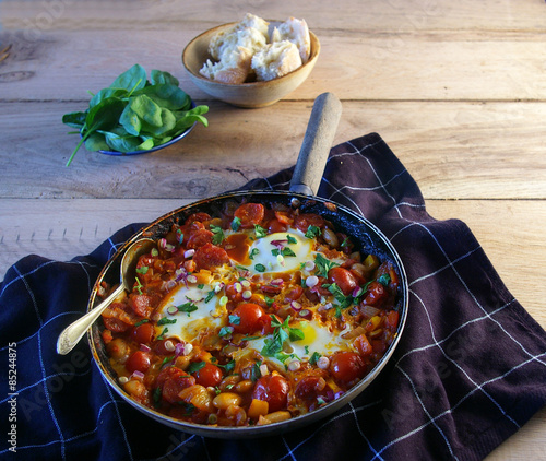 Spanish eggs presented in a frying pan with bread and spinach