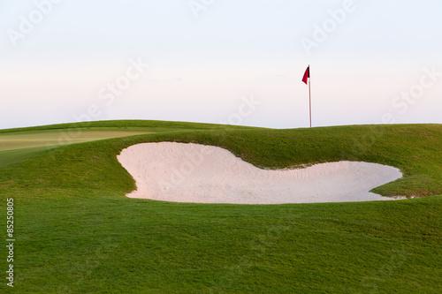 Sand bunker in front of golf green and flag