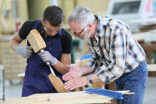 Foto Young apprentice with teacher working on piece of wood