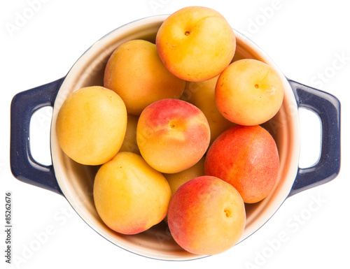 Ripe apricot fruits in a bliue pot over white background
