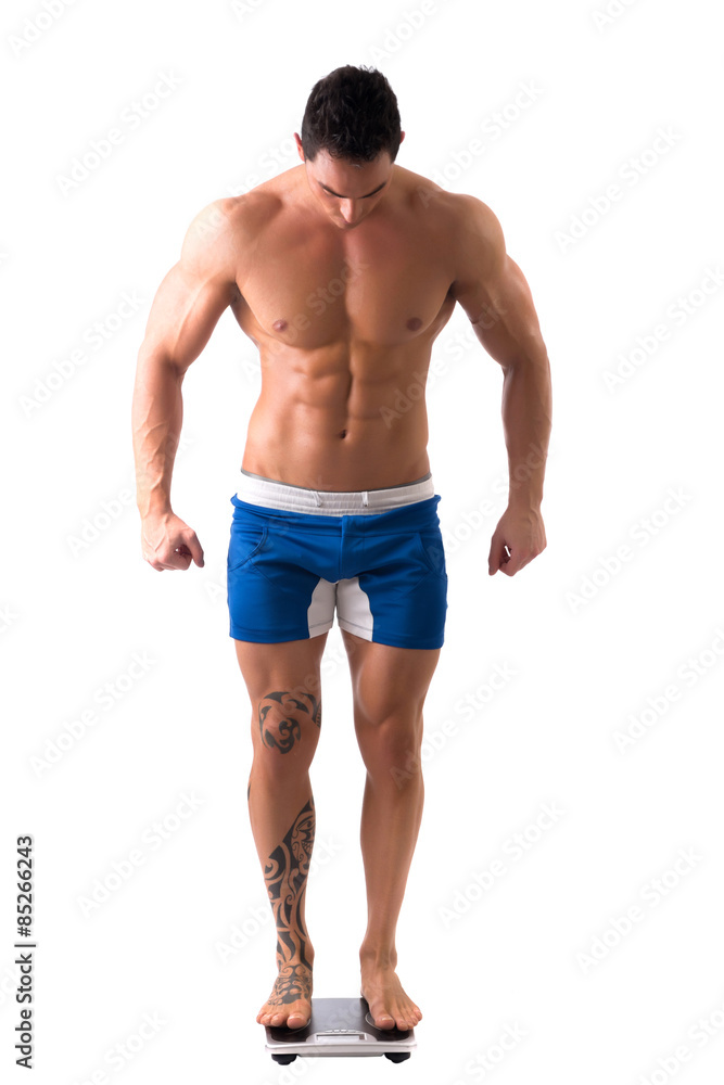 Muscular young man weighing himself on scale, making OK sign Muscular young man weighing himself on scale, making OK sign