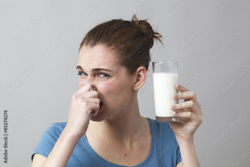 young woman not willing to drink a glass of smelly milk or disgusting white beverage young woman not willing to drink a glass of smelly milk or disgusting white beverage