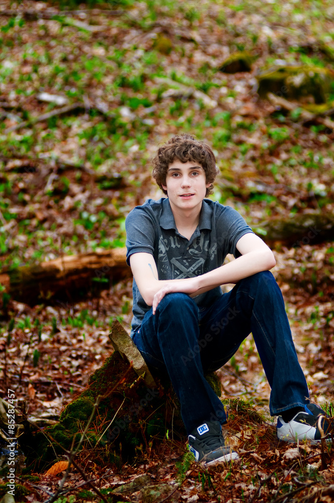 teen boy sitting outdoors in a forest teen boy sitting outdoors in a forest
